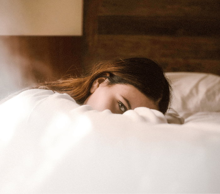 Eine Frau blickt über ihren Arm in die Kamera, während sie auf dem Bett im Lifestyle-Hotel liegt