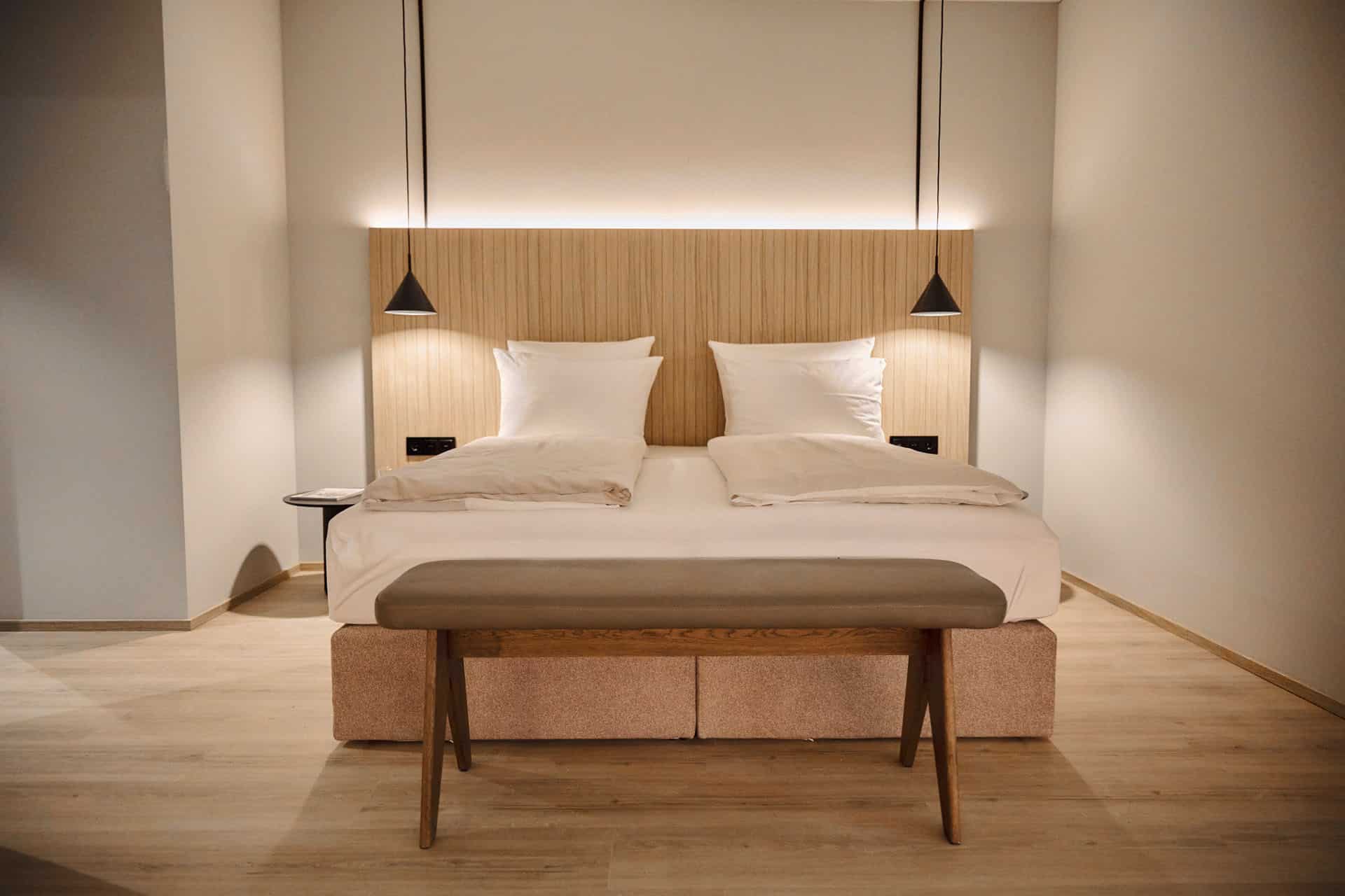 Ein Doppelbett, Nachtlampen und eine Bettbank im Lifestyle Hotel